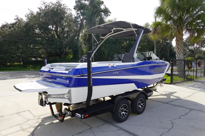Slide: The Image of 2024 Malibu 21 LX-R boat on trailer, blue and white, parked outdoors. - 2