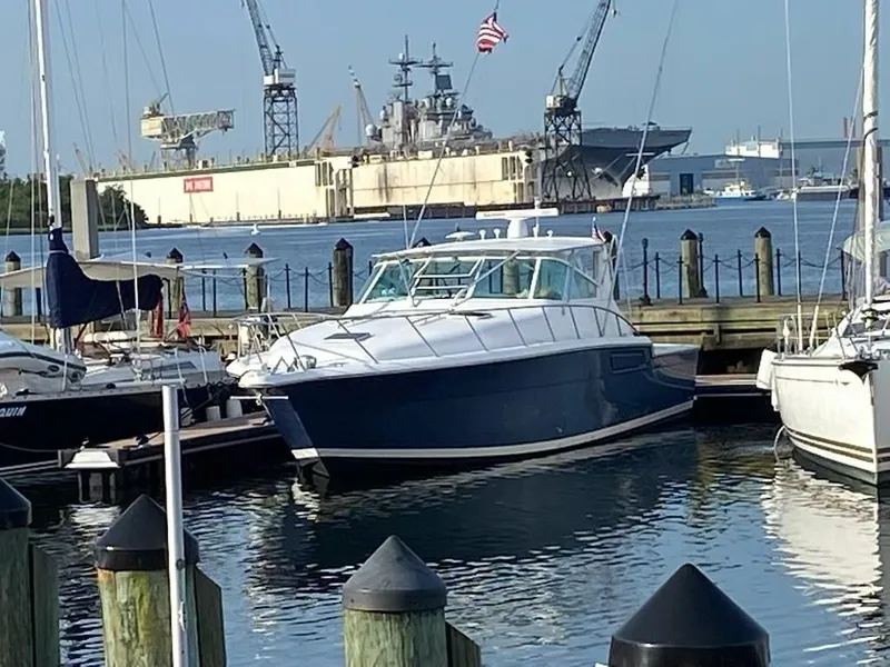 Slide: The Image of 1991 Tiara Yachts 4300 Open docked in a marina with shipyard background. - 5