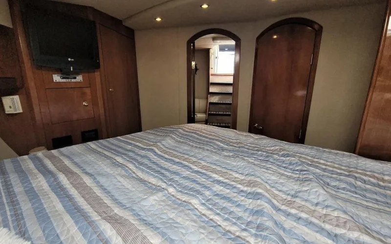 Slide: The Image of 2003 Cruisers Yachts 4370 Express cabin interior with bed, TV, and wooden doors. - 12