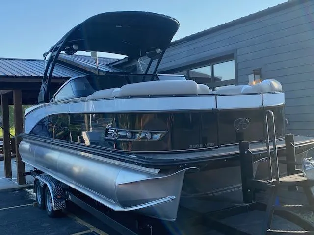 Slide: The Image of 2024 Avalon Catalina 2585 VRB pontoon boat on trailer, docked near a modern building. - 4