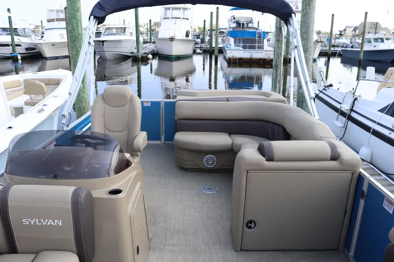 Slide: The Image of 2024 Sylvan Mirage 8520 Cruise pontoon boat interior at marina, featuring plush seating and helm. - 11