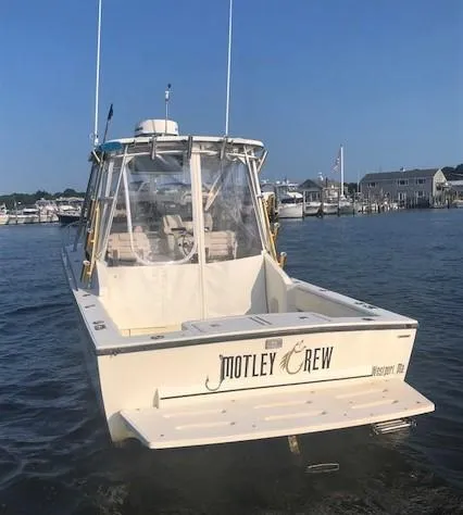 Slide: The Image of 2003 Carolina Classic 25 I/O boat named "Motley Crew" docked in a marina. - 2