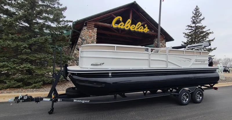 The Image of 2024 Ranger Reata 223C pontoon boat on trailer outside Cabela's store. - 0