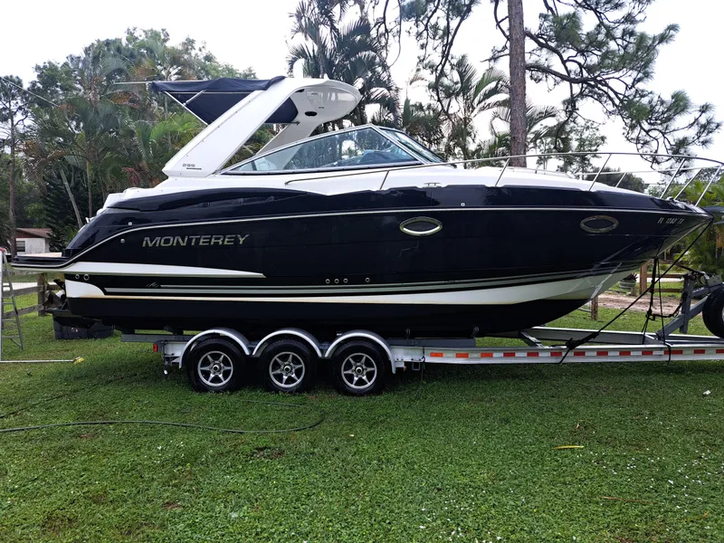 Slide: The Image of 2015 Monterey 295 Sport Yacht on a triple-axle trailer, parked on grass. - 2