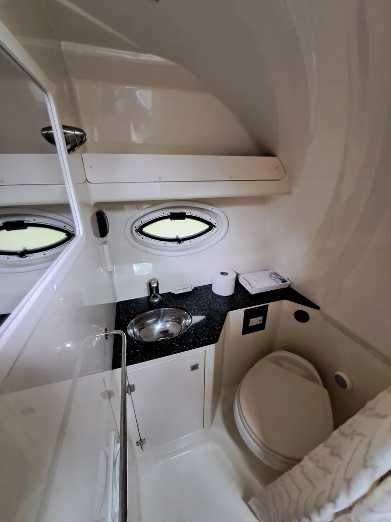 Slide: The Image of 2015 Monterey 295 Sport Yacht bathroom with sink, toilet, and porthole windows. - 27