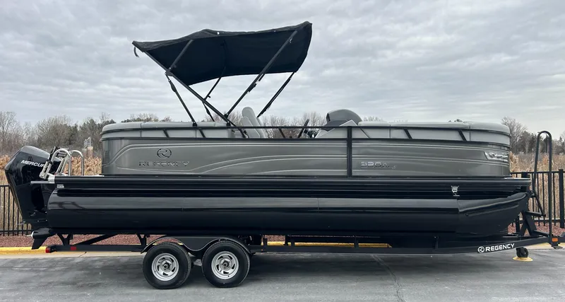 The Image of 2024 Regency 230 DL3 pontoon boat on a trailer with a black canopy. - 0