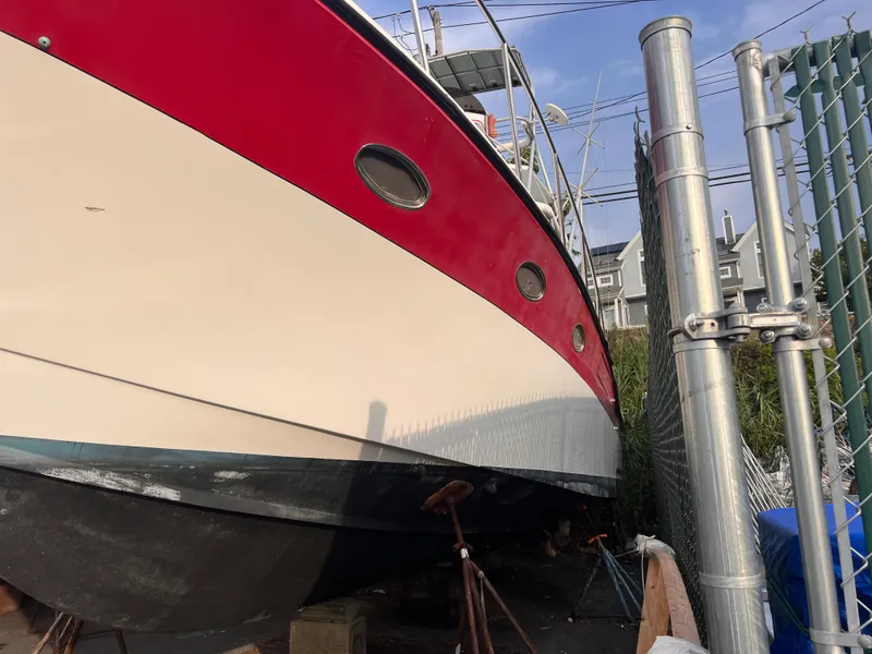 Slide: The Image of 1988 Canyon Bay 40 boat with red and white hull, docked near a metal fence. - 5