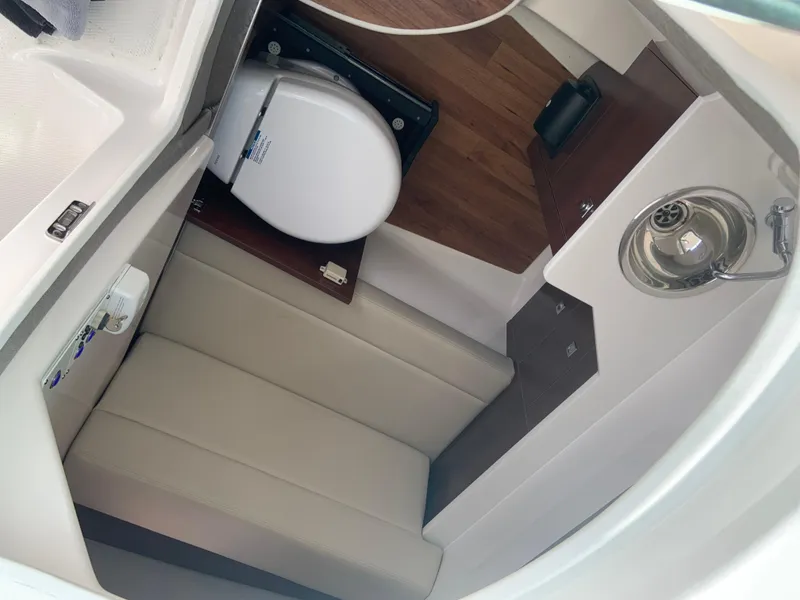 Slide: The Image of 2020 Chaparral 280 OSX boat interior with toilet, sink, and cushioned seating. - 22