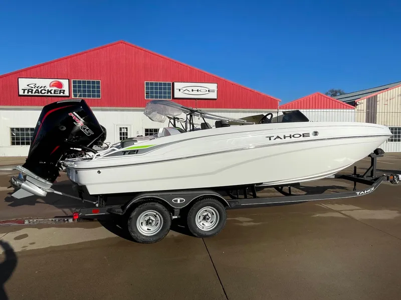 The Image of 2024 Tahoe T21 boat on trailer, parked outside red building under clear blue sky. - 0
