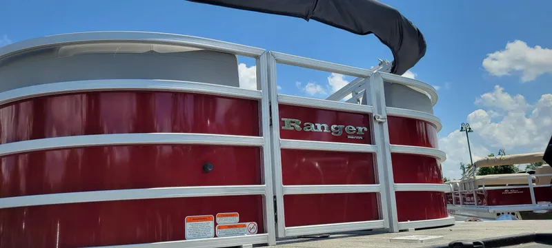 Slide: The Image of 2024 Ranger Reata 243C pontoon boat with red exterior, under a clear blue sky. - 3