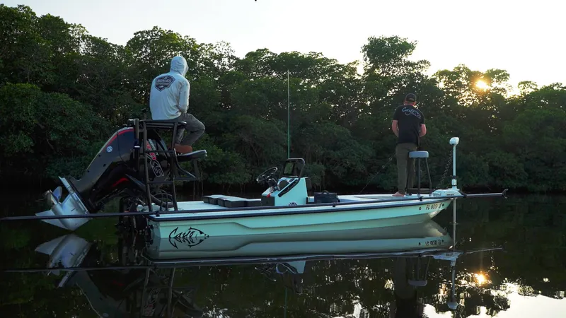 Slide: The Image of 2024 Cayo Boatworks 180 skiff with two anglers in a serene, wooded waterway at sunrise. - 5