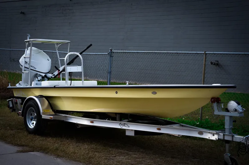 Slide: The Image of 2024 Cayo Boatworks 173 on trailer, yellow hull, outboard motor, parked by chain-link fence. - 19
