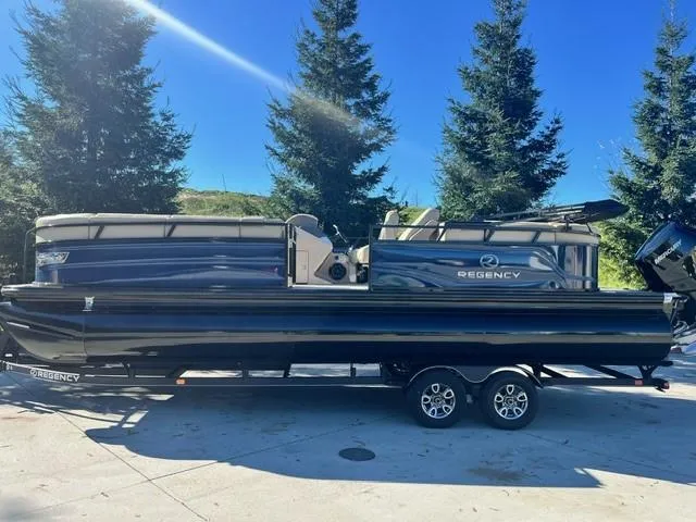 Slide: The Image of 2024 Regency 250 LE3 pontoon boat on a trailer, parked outdoors. - 0