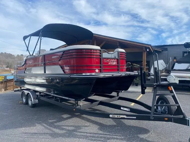 Slide: The Image of 2024 SunCatcher Elite 324 SS pontoon boat on a trailer, red and black design. - 2