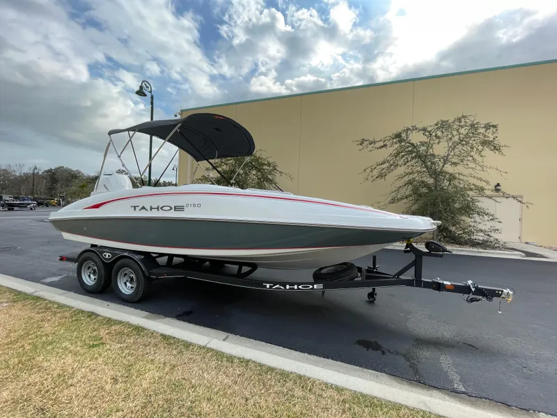 Slide: The Image of 2024 Tahoe 2150 boat on trailer with canopy, parked outdoors. - 2
