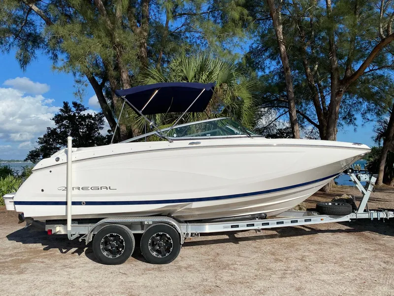 Slide: The Image of 2017 Regal 22 FasDeck boat on a trailer, parked outdoors with trees in the background. - 10
