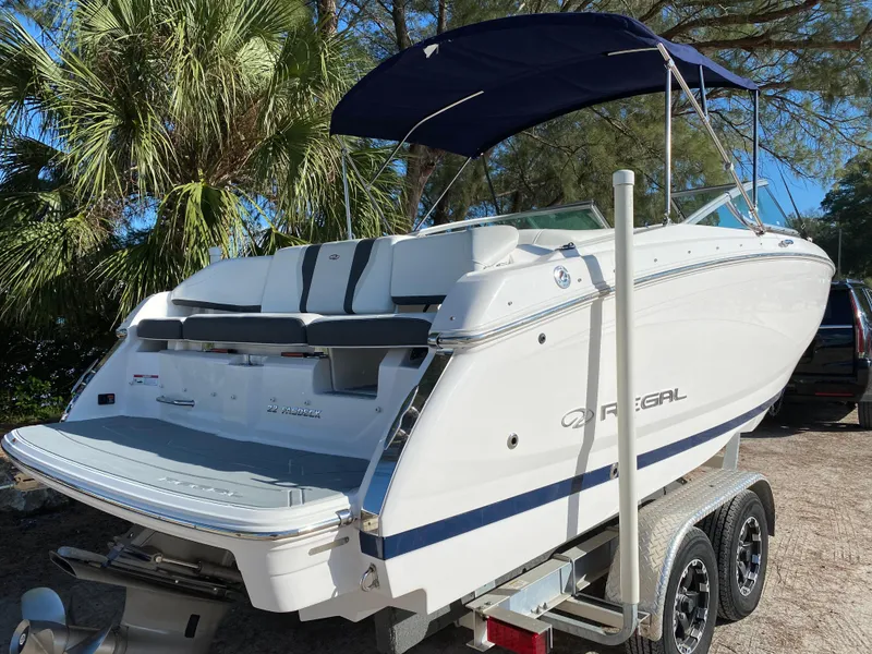 Slide: The Image of 2017 Regal 22 FasDeck boat with blue canopy on trailer, parked near palm trees. - 7