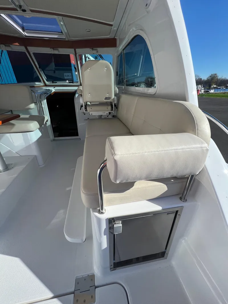 Slide: The Image of 2017 Back Cove Downeast 37 interior seating area with white upholstery and storage compartment. - 27