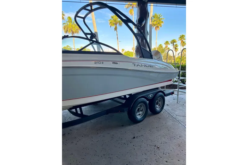 Slide: The Image of 2024 Tahoe 210 S boat on trailer, parked outdoors with palm trees in the background. - 11
