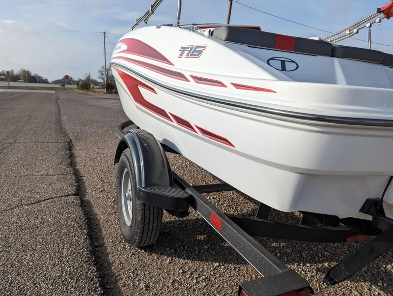 Slide: The Image of 2024 Tahoe T16 boat on trailer, white with red accents, parked on a road. - 4