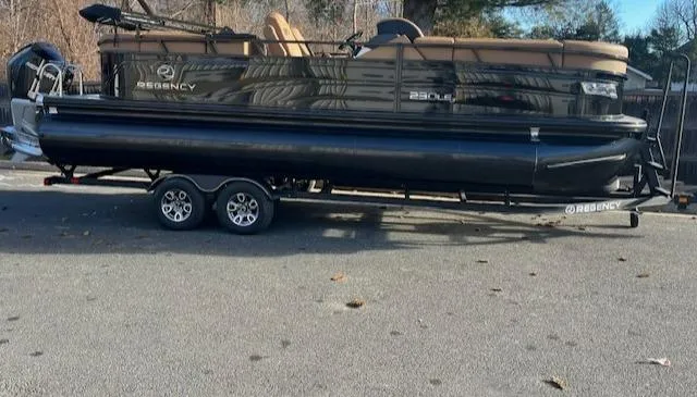 Slide: The Image of 2024 Regency 230 LE3 pontoon boat on a trailer in a parking lot. - 1