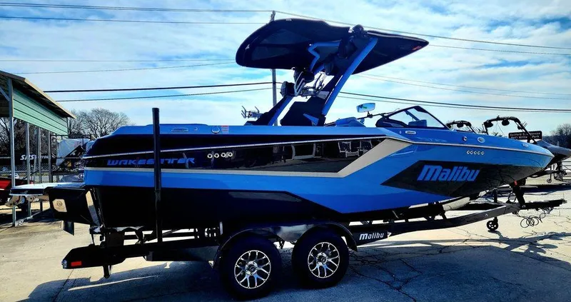Slide: The Image of 2024 Malibu 23 MXZ wakeboard boat in blue and black on a trailer. - 14