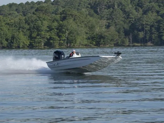 Slide: The Image of 2024 Xpress Boats X21 PRO speeding on a lake with forested background. - 1