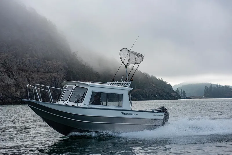 Slide: The Image of 2023 Spartan 220 Maximus Pro boat cruising on misty water near rocky shore. - 16