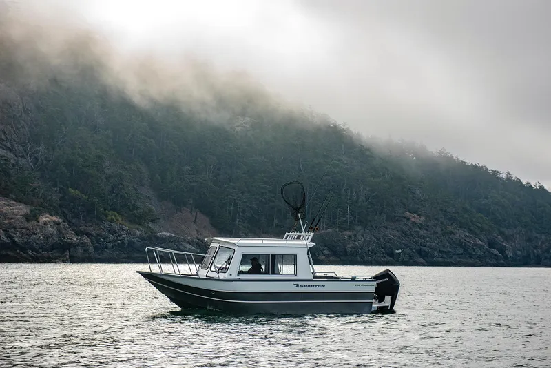 Slide: The Image of 2023 Spartan 220 Maximus Pro boat cruising near a misty forested shoreline. - 17