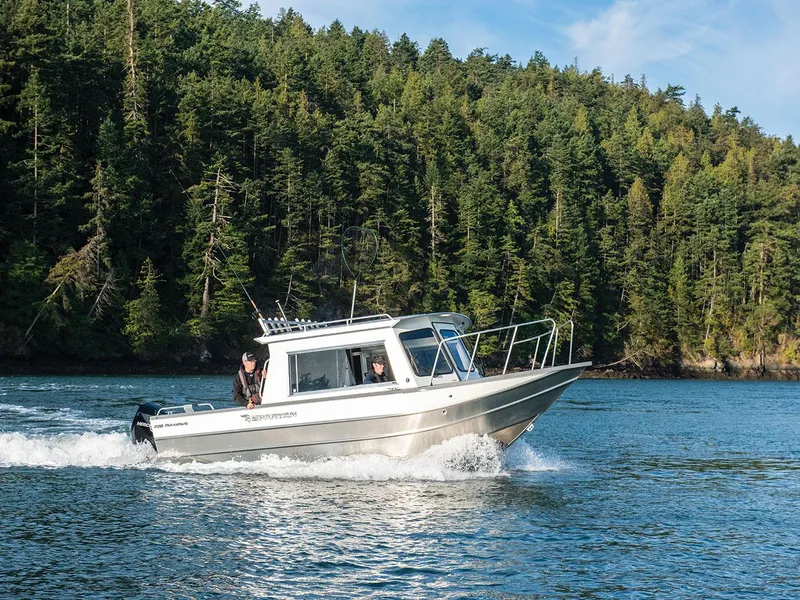 Slide: The Image of 2023 Spartan 220 Maximus Pro boat cruising on a lake with forested background. - 18