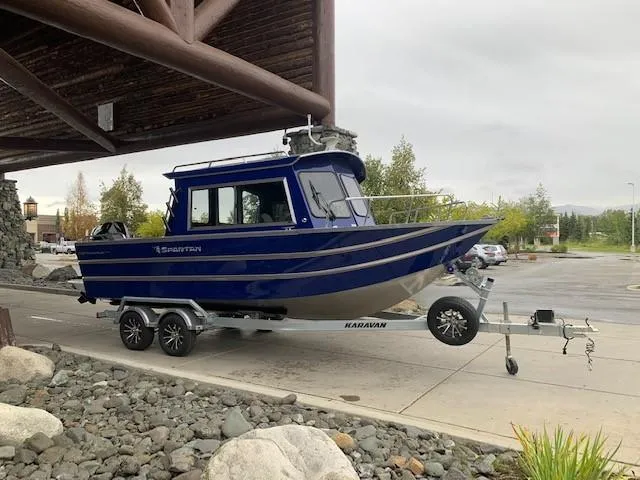 Slide: The Image of 2023 Spartan 220 Maximus Pro boat on Karavan trailer, parked under wooden structure. - 2