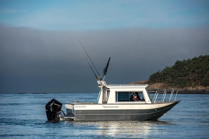 Slide: The Image of 2023 Spartan 220 Maximus Pro boat on calm water near forested shoreline. - 22