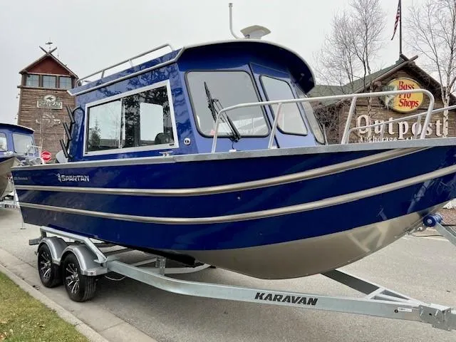 Slide: The Image of 2023 Spartan 220 Maximus Pro boat on Karavan trailer, parked near a rustic building. - 6
