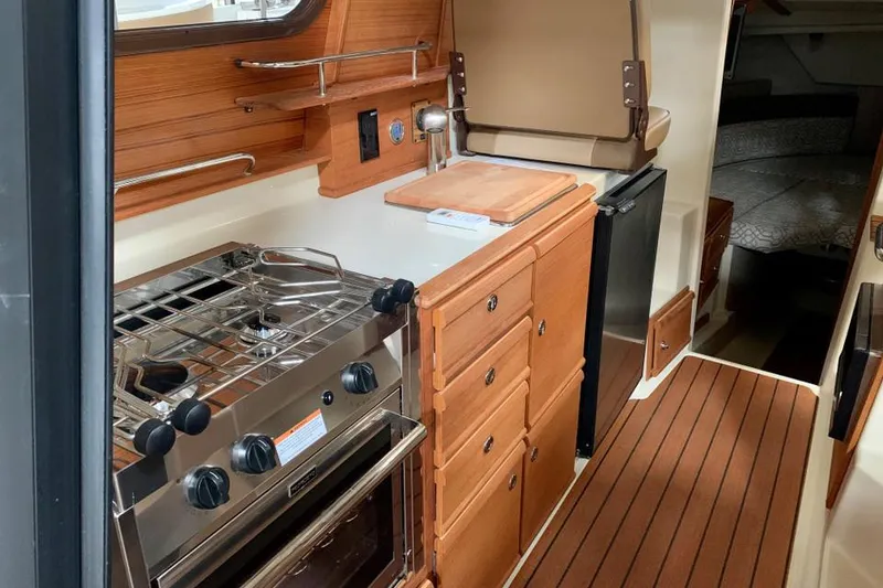 Slide: The Image of 2022 Ranger Tugs R-27 interior kitchen with stove, wooden cabinets, and refrigerator. - 7