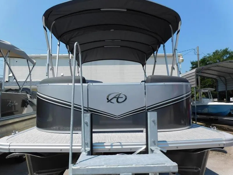 Slide: The Image of 2023 Avalon 2385 LSZ VRL pontoon boat with canopy, docked under clear blue sky. - 2