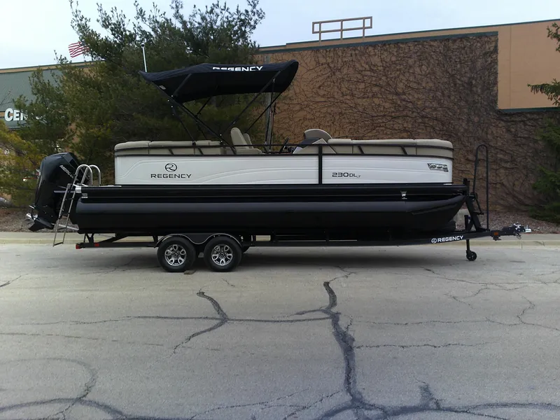 The Image of 2024 Regency 230 DL3 pontoon boat on a trailer, parked outdoors. - 0
