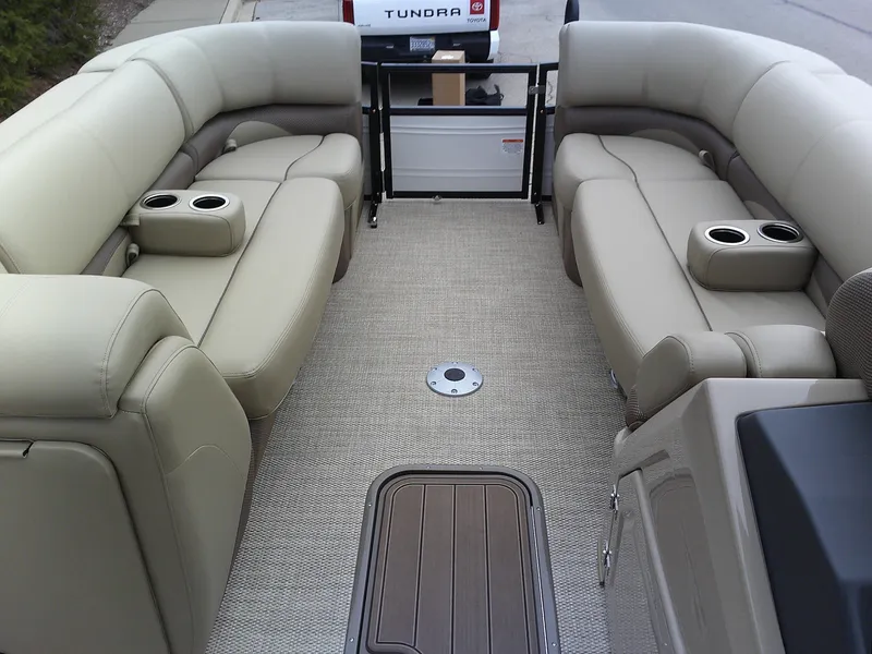 Slide: The Image of 2024 Regency 230 DL3 pontoon boat interior with beige seating and cup holders. - 2