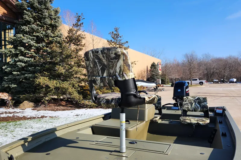 Slide: The Image of 2024 Tracker Grizzly 1754 SC boat with camo seats, parked outdoors. - 2