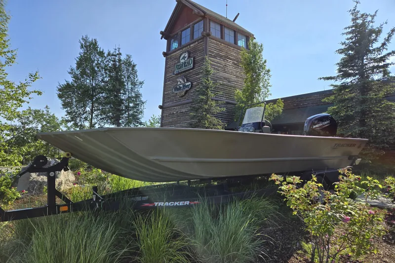 Slide: The Image of 2024 Tracker Grizzly 2072 CC boat displayed outdoors near a rustic building. - 2