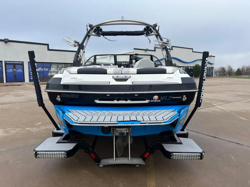 Slide: The Image of 2018 Malibu 21 VLX boat, rear view, parked on concrete, showcasing sleek design and features. - 3