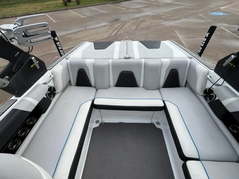 Slide: The Image of 2018 Malibu 21 VLX boat interior with white and black seating, cup holders, and wakeboard racks. - 7