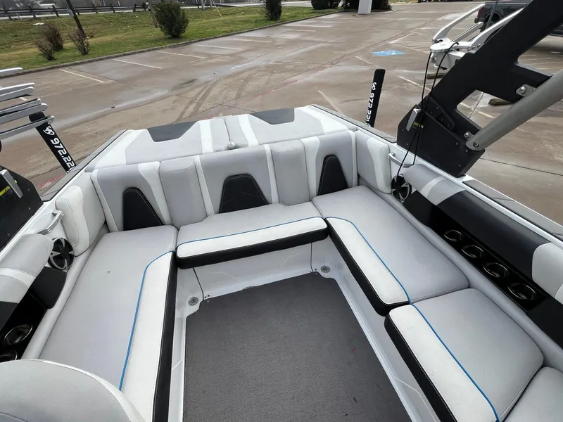 Slide: The Image of 2018 Malibu 21 VLX boat interior with white and black seating, parked outdoors. - 9