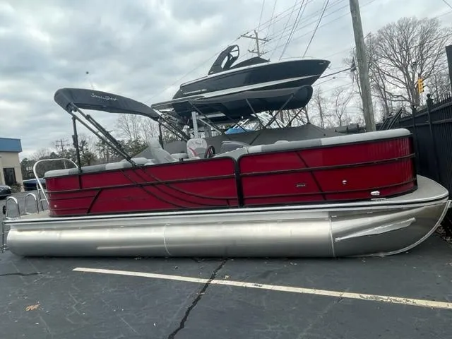 Slide: The Image of 2023 South Bay 224 RS 3.0 pontoon boat in red, parked on pavement. - 1
