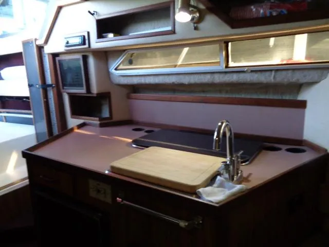 Slide: The Image of 1986 Sea Ray 250 Sundancer boat interior kitchen with sink, cutting board, and storage. - 4