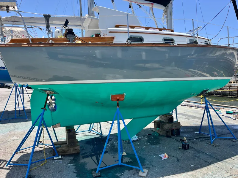 Slide: The Image of 1985 Cape Dory 270 sailboat on stands, gray hull, turquoise bottom, marina setting. - 12