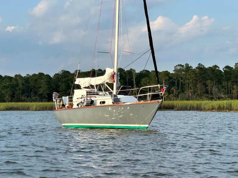 Slide: The Image of 1985 Cape Dory 270 sailboat anchored on calm water near a forested shoreline. - 4