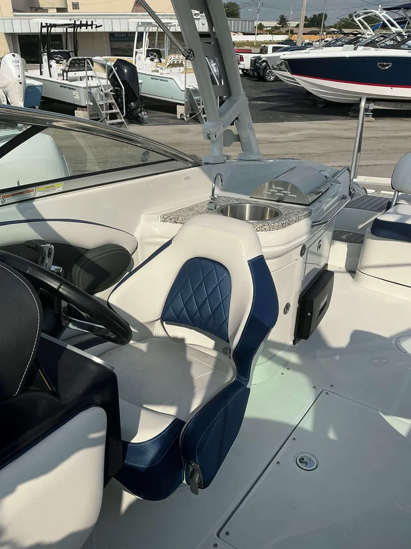 Slide: The Image of 2024 Crownline 290 XS boat interior with blue and white seating and a compact kitchenette. - 8