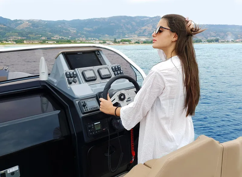 Slide: The Image of Woman steering Ranieri CAYMAN 28 EXECUTIVE boat, 2025 model, on a scenic coastal waterway. - 9