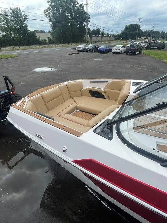 Slide: The Image of 2024 Moomba Tykon boat with tan seating and red accents, parked outdoors. - 46