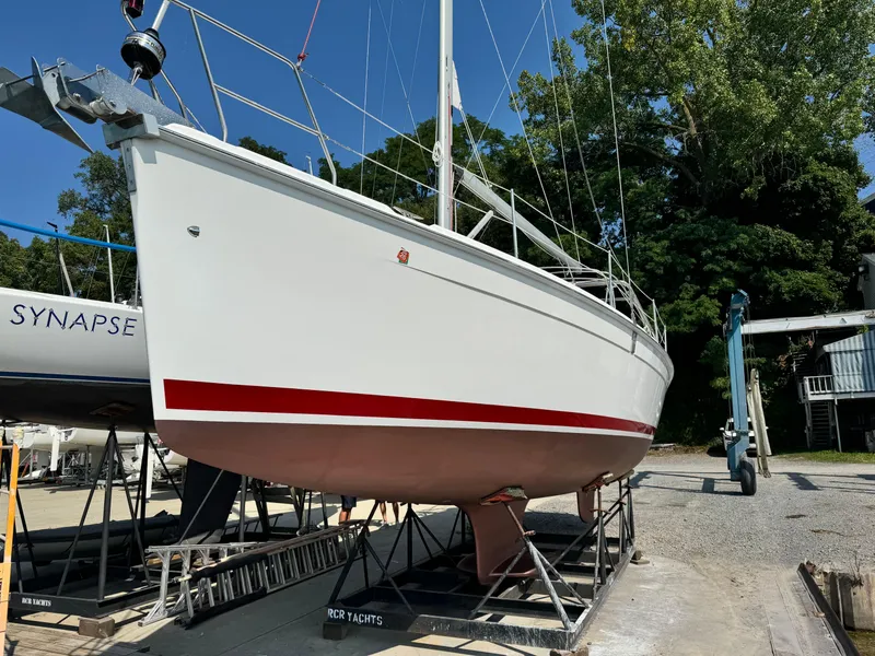 Slide: The Image of 2005 Hunter 38 sailboat on dry dock, white hull with red stripe, surrounded by trees. - 2